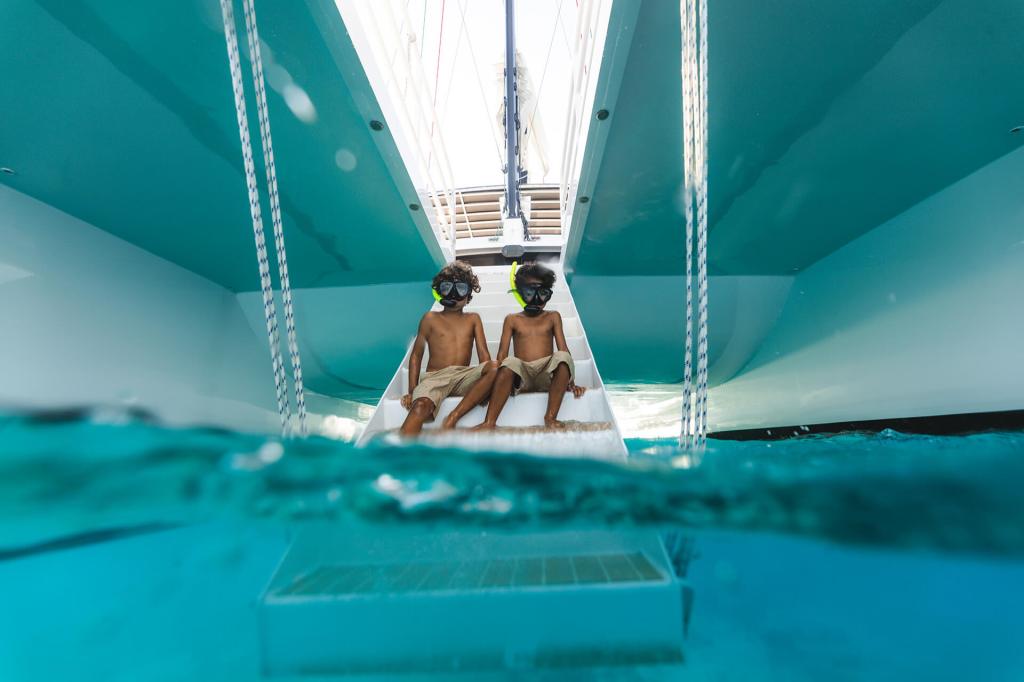 Two kids wearing goggles sitting on a boat slide above water.