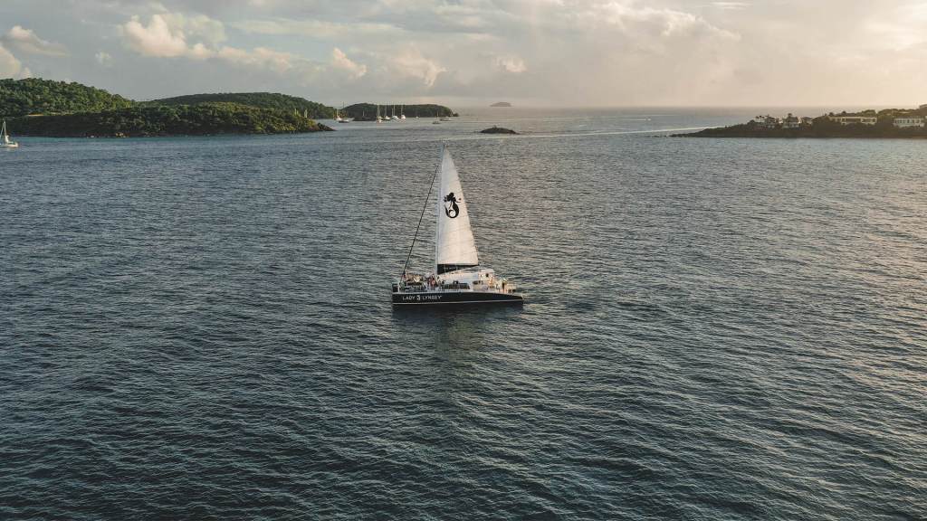Sailboat on calm sea with islands in the background under a cloudy sky.