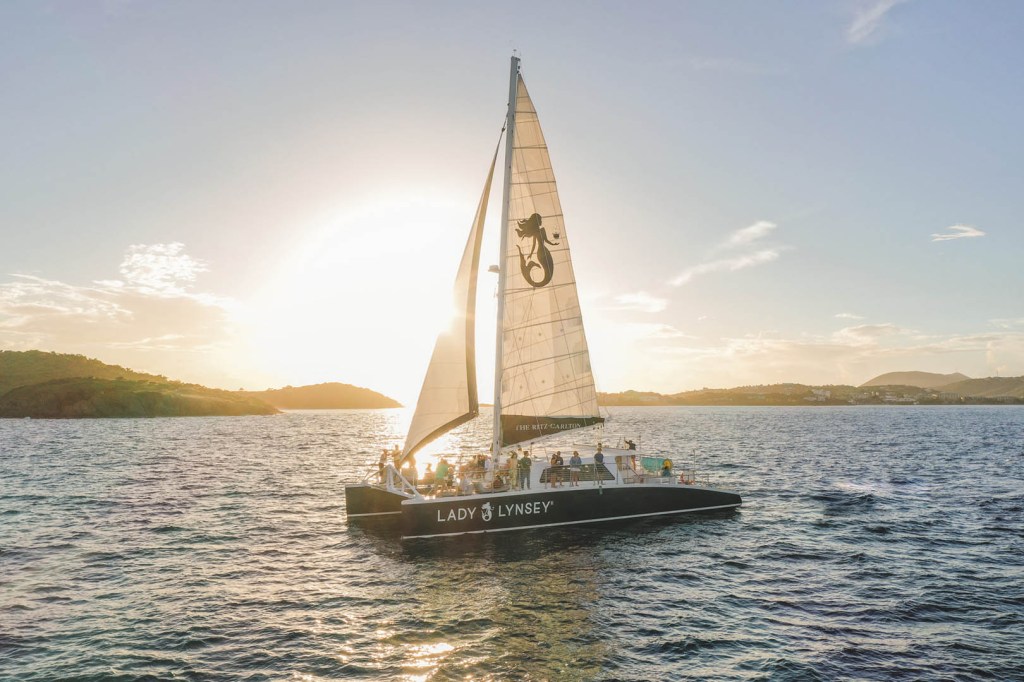Sailboat on the water at sunset with people onboard and islands in the background.