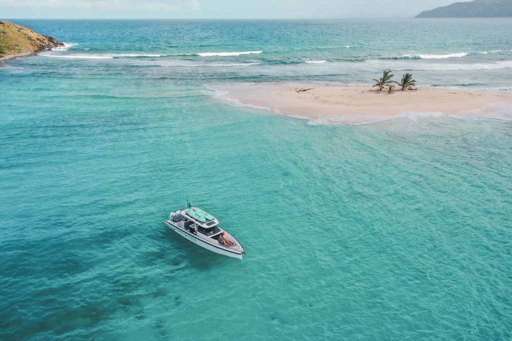 Boat on turquoise water near a sandy island with palm trees.