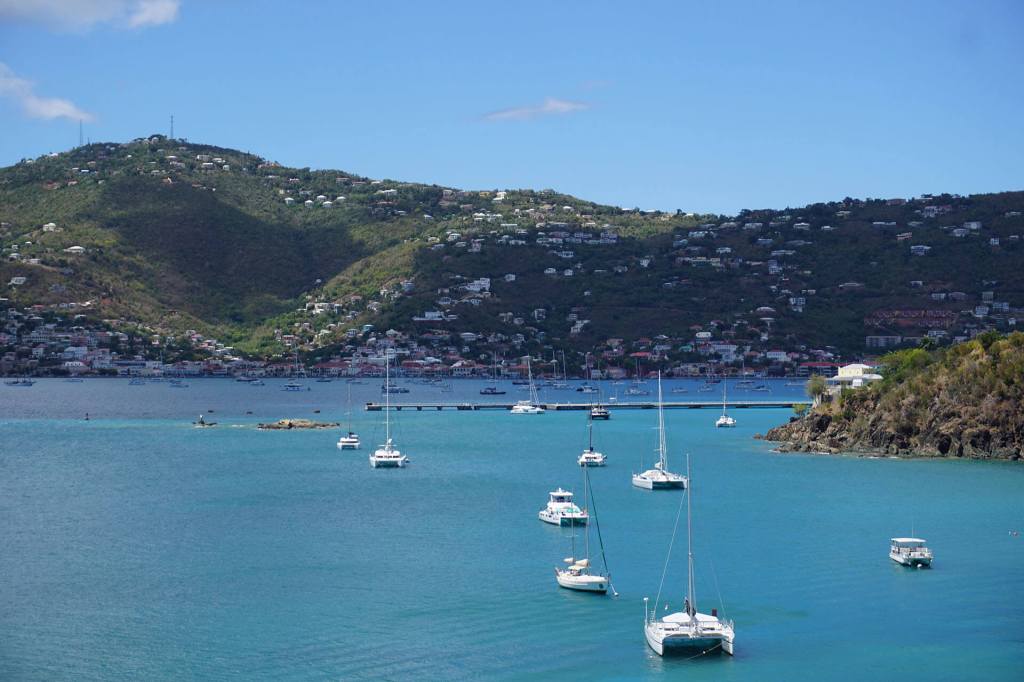 Boats anchored in a blue bay with mountains and clear sky in the background.