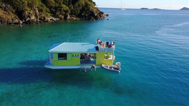 People on a floating yellow bar in clear blue water, with a small boat nearby.