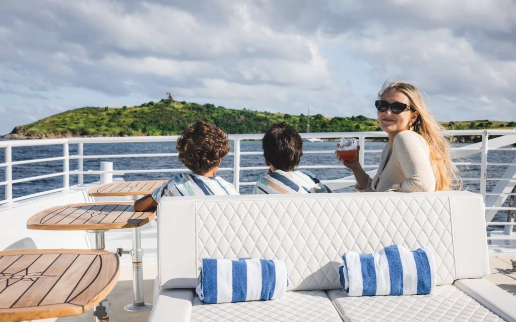 Woman with drink and two kids on boat, island in background.