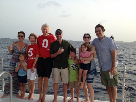 Group of adults and children smiling on a boat with ocean background.