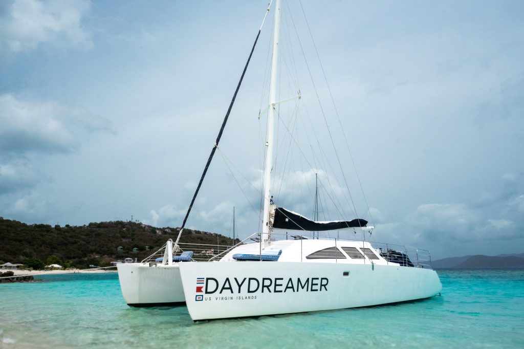 Catamaran named 'Daydreamer' docked on a turquoise beach.